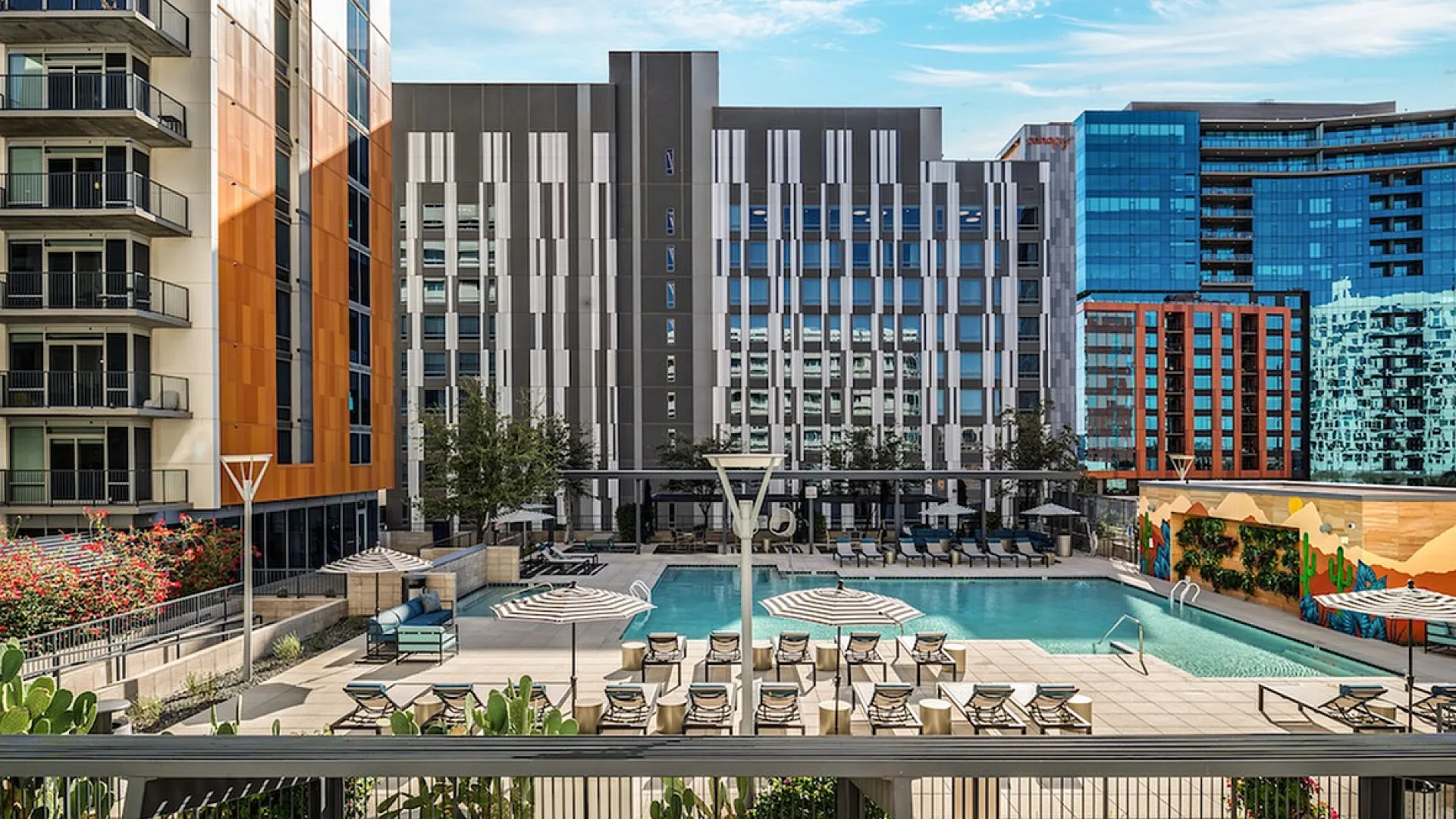 Modern urban apartment complex with a luxurious outdoor pool area, stylish lounge chairs, and vibrant cityscape backdrop.