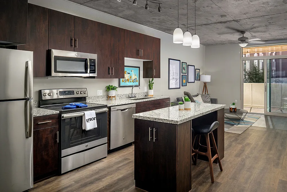 Modern open-concept kitchen with granite countertops, stainless steel appliances, and chic decor, leading to a cozy living area with natural light.