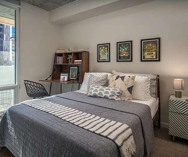 Bright and cozy bedroom with a stylish bed, elegant desk, and a sunlit window offering cityscape views.
