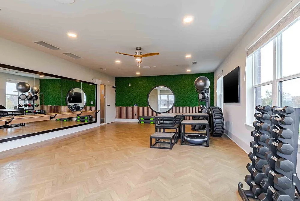 Modern fitness room with stylish wood flooring, full-length mirrors, vibrant green accent wall, and well-equipped with free weights and exercise gear.