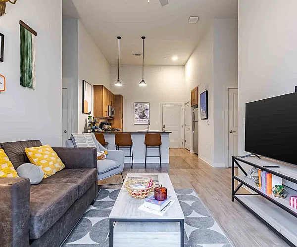 Chic open-plan living room with contemporary decor, featuring a cozy couch, vibrant cushions, and a sleek kitchen island with stylish bar stools.