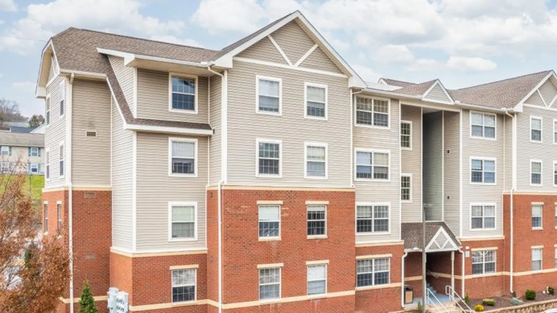 Modern apartment complex with attractive brick and siding exterior, ample parking, and a welcoming entrance under a bright blue sky.