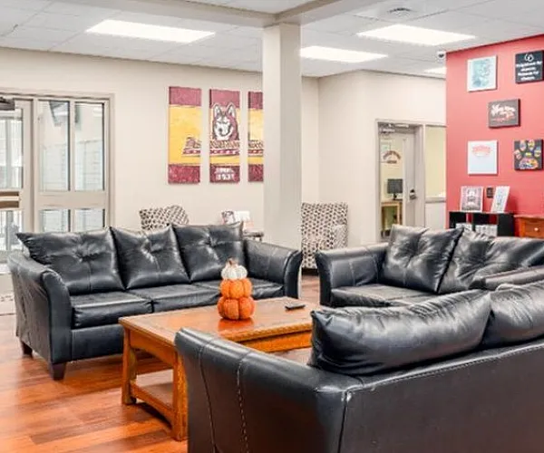 Welcoming lobby area featuring plush black leather sofas, warm wood floors, and vibrant wall art, creating a cozy atmosphere for residents.