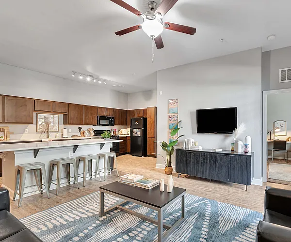 Modern and inviting open-plan living area featuring a sleek kitchen with wooden cabinetry, spacious bar seating, and a cozy living room with a contemporary design. Light-filled space perfect for relaxation and entertaining.