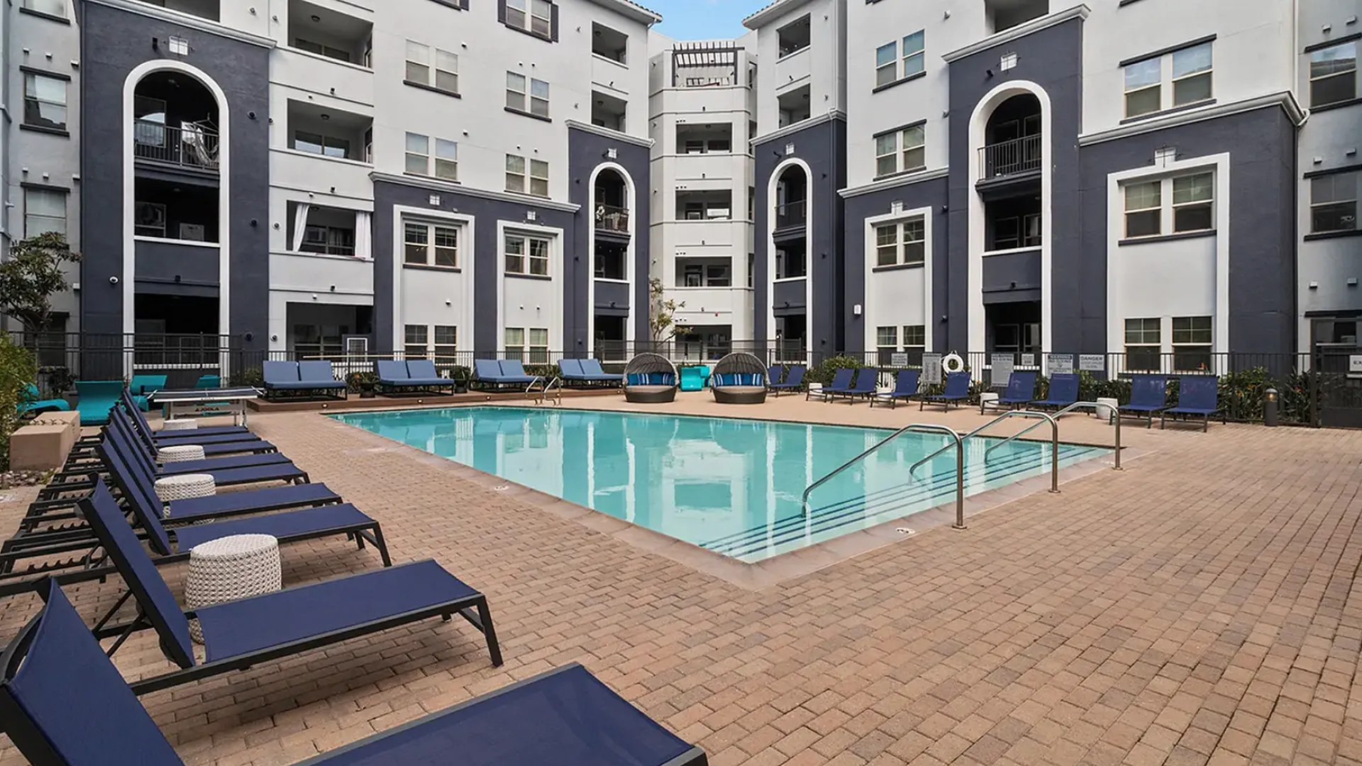 Contemporary apartment complex featuring a stunning outdoor pool area with luxurious lounge chairs and upscale architecture.
