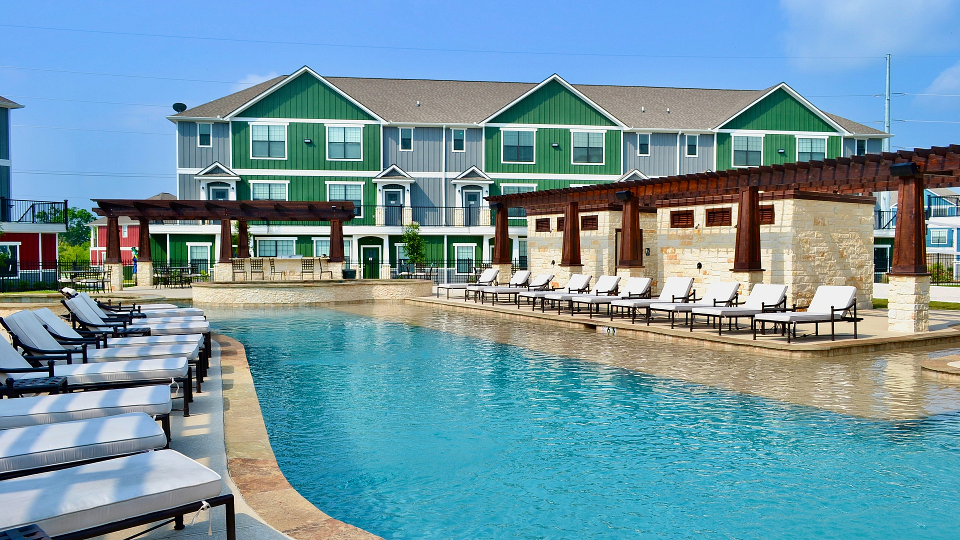 Charming apartment complex with a pristine swimming pool, surrounded by modern lounge chairs and greenery, offering a relaxing retreat.