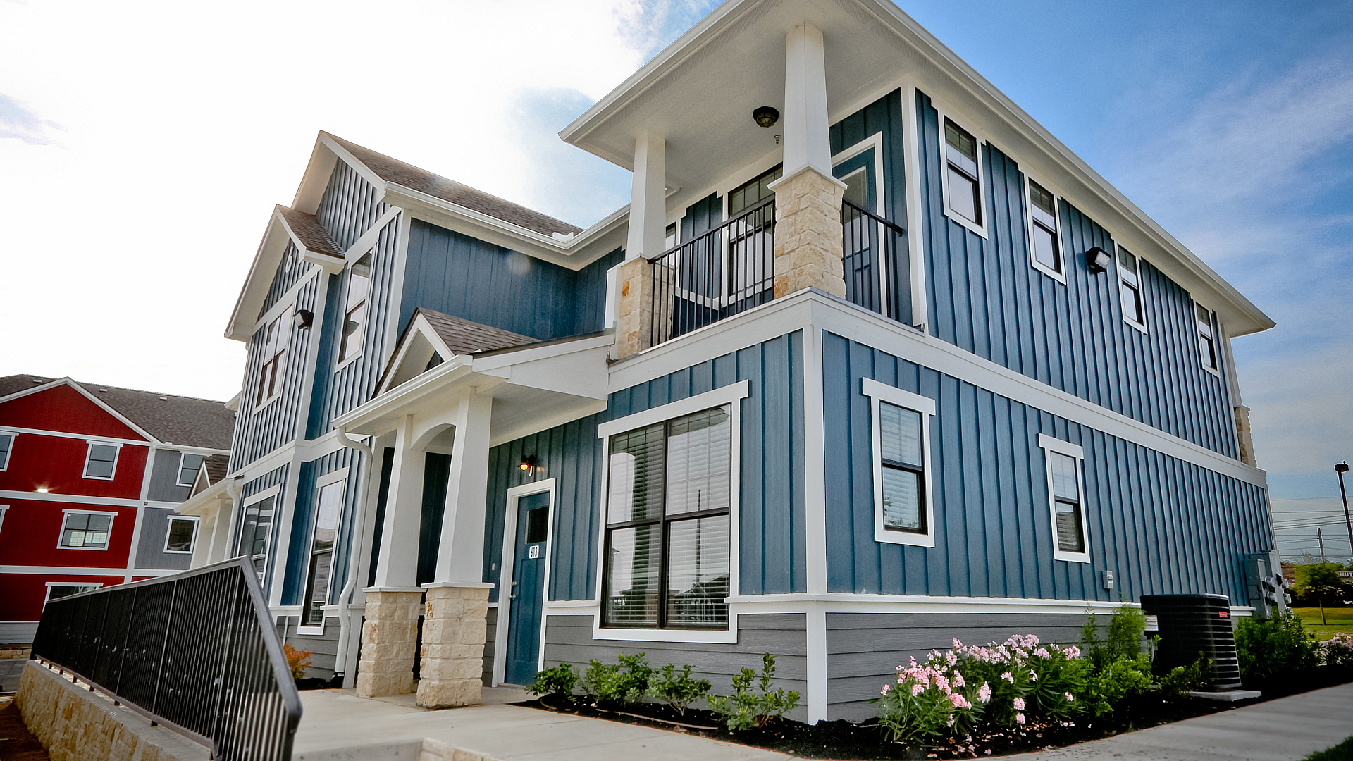 Charming two-story blue house with elegant white accents, featuring a welcoming porch and blooming garden, perfect for modern living.