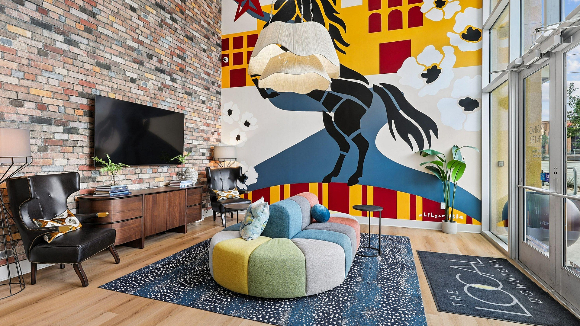 Vibrant lounge area with eclectic mural, modern furnishings, and natural light streaming through large windows.