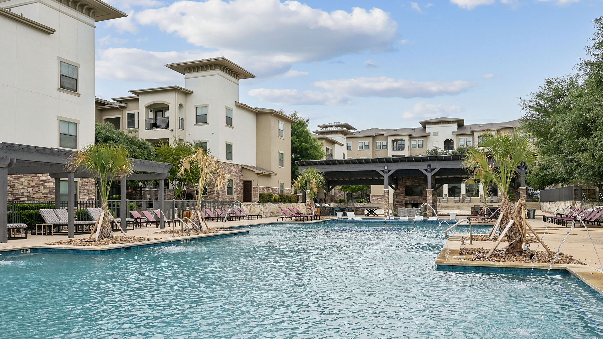 Luxurious apartment complex showcasing a sparkling swimming pool surrounded by elegant lounge chairs and lush palm trees, offering a serene outdoor escape.