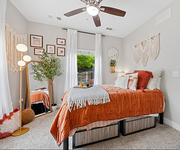 Cozy bedroom with orange accents, stylish wall art, and a large mirror reflecting natural light.
