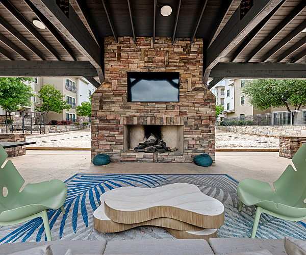 Chic outdoor lounge with modern seating, rustic stone fireplace, and a mounted TV, perfect for relaxation and entertainment.