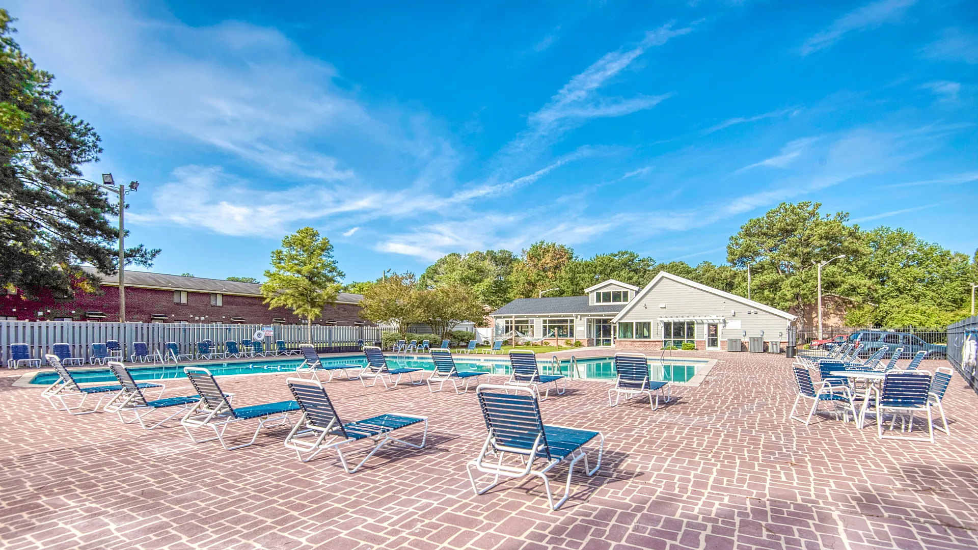 Inviting outdoor pool area with numerous lounge chairs, set against a backdrop of lush trees and a modern clubhouse.