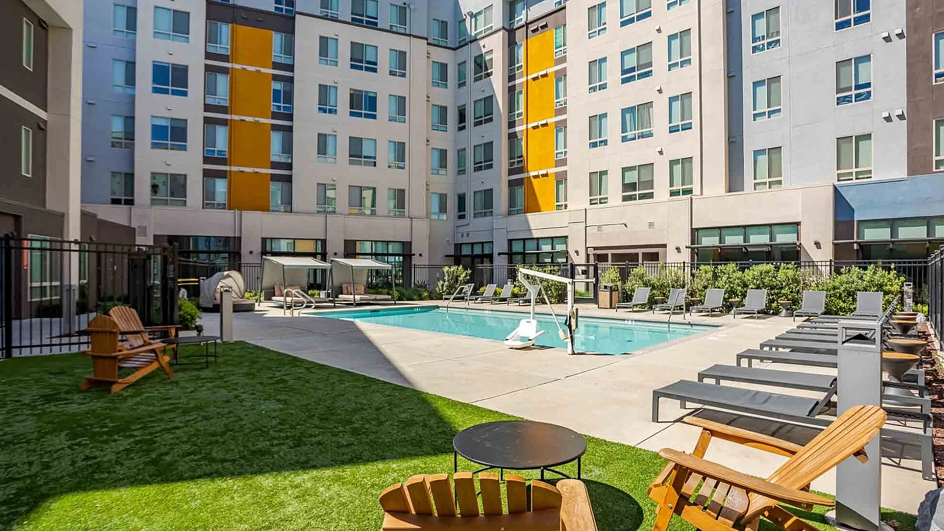 Modern apartment complex showcasing a vibrant outdoor pool area with ample seating and immaculate greenery.