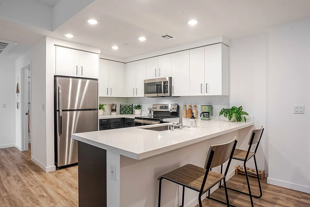 Modern kitchen with sleek white cabinetry, stainless steel appliances, and a spacious breakfast bar with stylish seating.