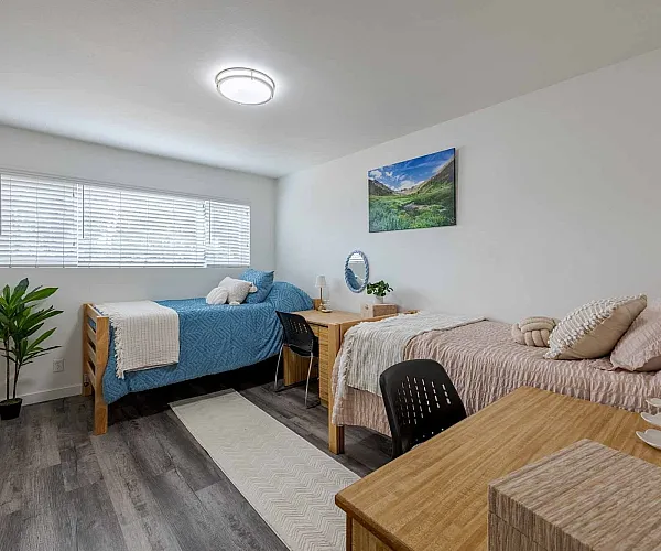 Bright and inviting bedroom with two cozy twin beds, modern decor, and a large window for natural light.