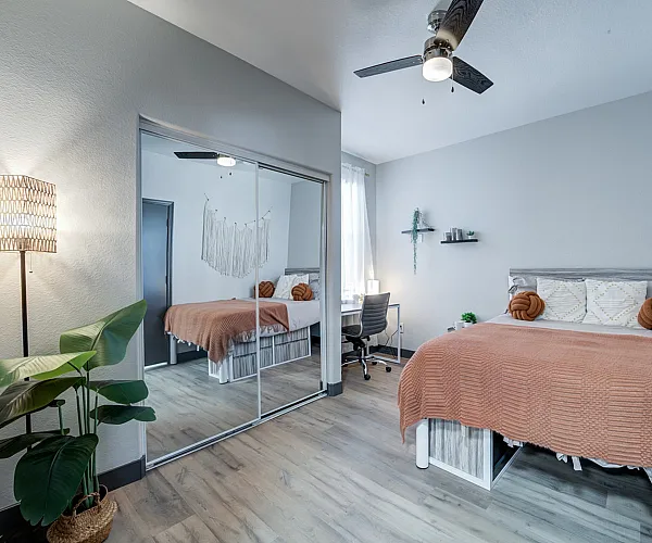 Inviting modern bedroom with stylish decor, featuring a cozy double bed with a soft orange blanket, elegant wall art, and ample natural light through sheer curtains.