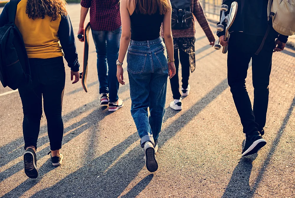 Group of young adults walking together on a sunny day, carrying skateboards and sharing a sense of unity and adventure.
