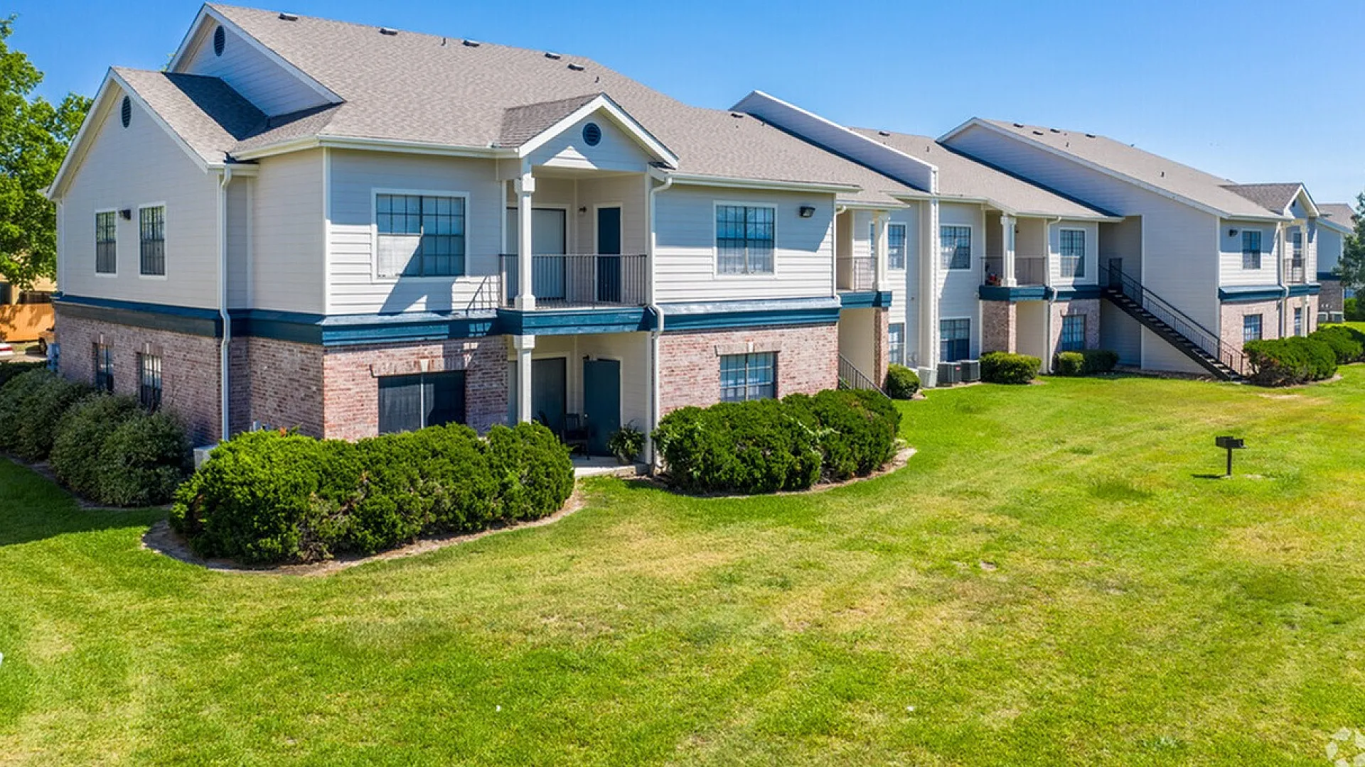 Charming two-story apartment complex with modern architecture, surrounded by lush greenery and clear blue skies, offering serene and spacious living.