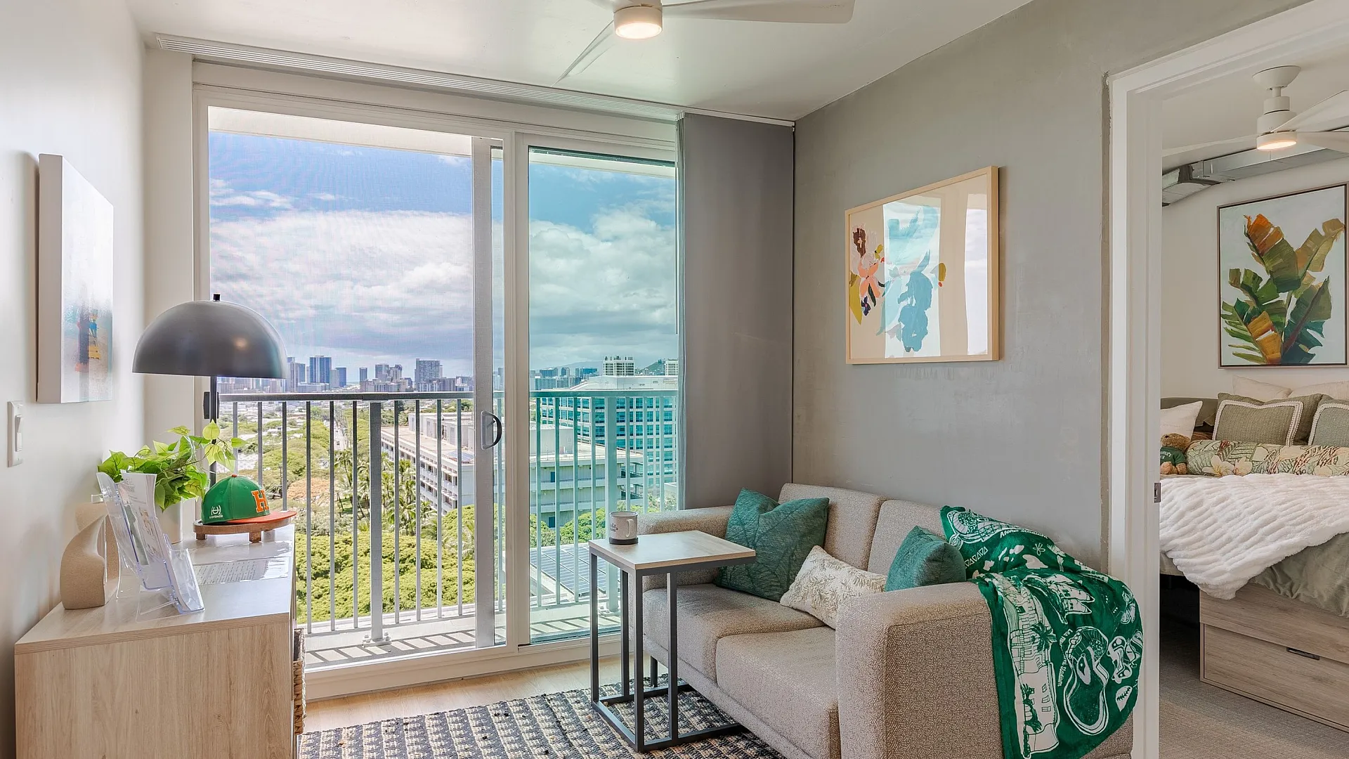 Bright urban apartment living room with cozy couch, stylish decor, and stunning cityscape views through sliding glass doors.