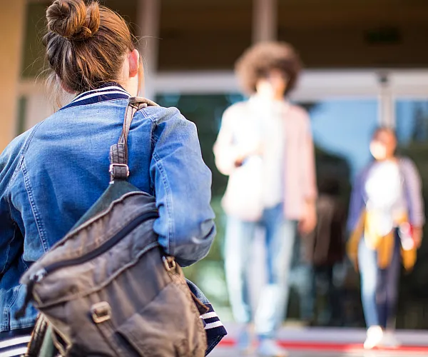 Vibrant outdoor scene with three people in casual attire, one in focus with a denim jacket and backpack, offers a welcoming atmosphere with blurred background.