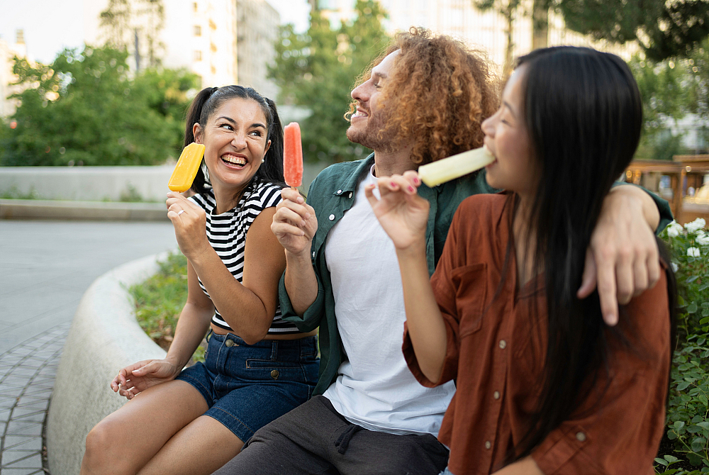 Joyful friends enjoying colorful popsicles outdoors, surrounded by greenery and warm smiles.