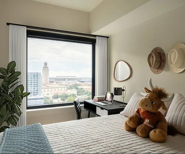 Bright bedroom with city view, decorated with hats and a cozy plush toy on the bed, featuring a modern desk setup.
