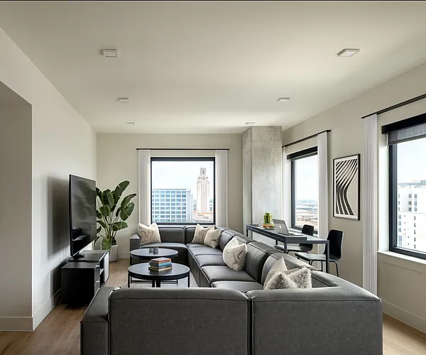 Modern living room with a sleek grey sectional sofa, large windows offering stunning city views, contemporary artwork, and a cozy workspace.
