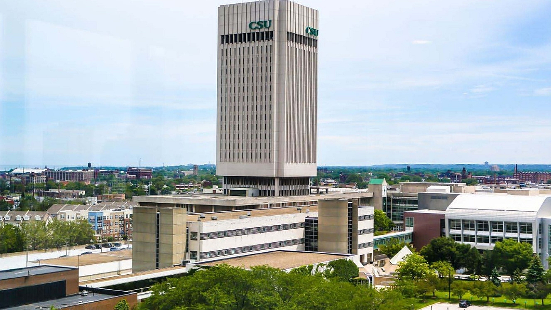 Panoramic view of modern cityscape with a prominent high-rise building and lush green surroundings.