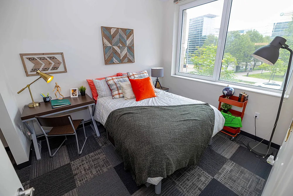 Chic and modern bedroom with a cozy bed adorned with vibrant cushions, stylish workspace with a sleek desk, and large window offering a stunning view of greenery outside.