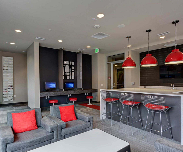 Modern communal space featuring stylish red and gray seating, high-tech workstations, and a sleek bar area with vibrant lighting.