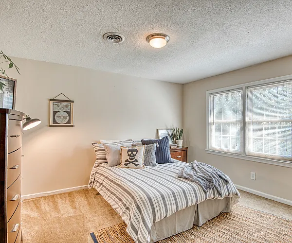 Cozy bedroom with a stylish striped bedspread, natural light pouring through large windows, and elegant decor accents.