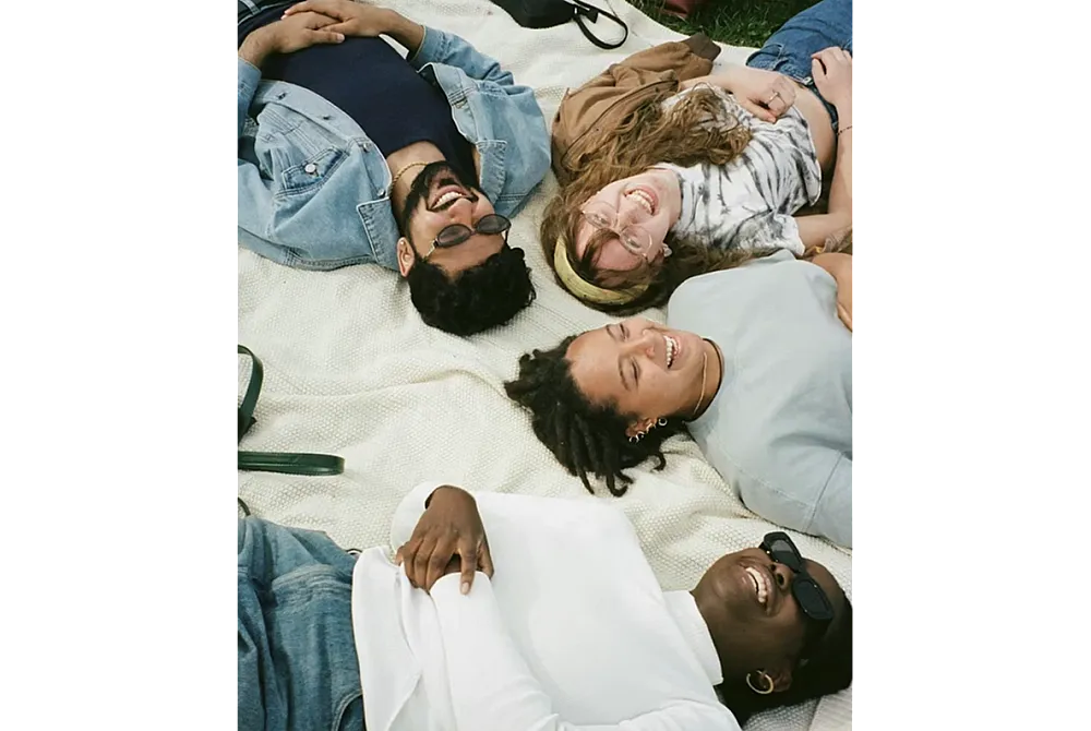 Joyful group of friends lying on a picnic blanket, enjoying a sunny day outdoors.