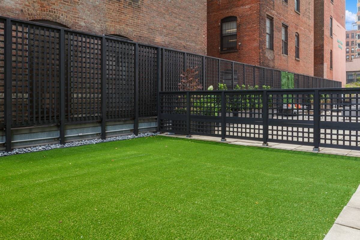 A fenced in astroturf area at our apartments in Manhattan, featuring a view of the outdoor lounge with cushioned chairs.