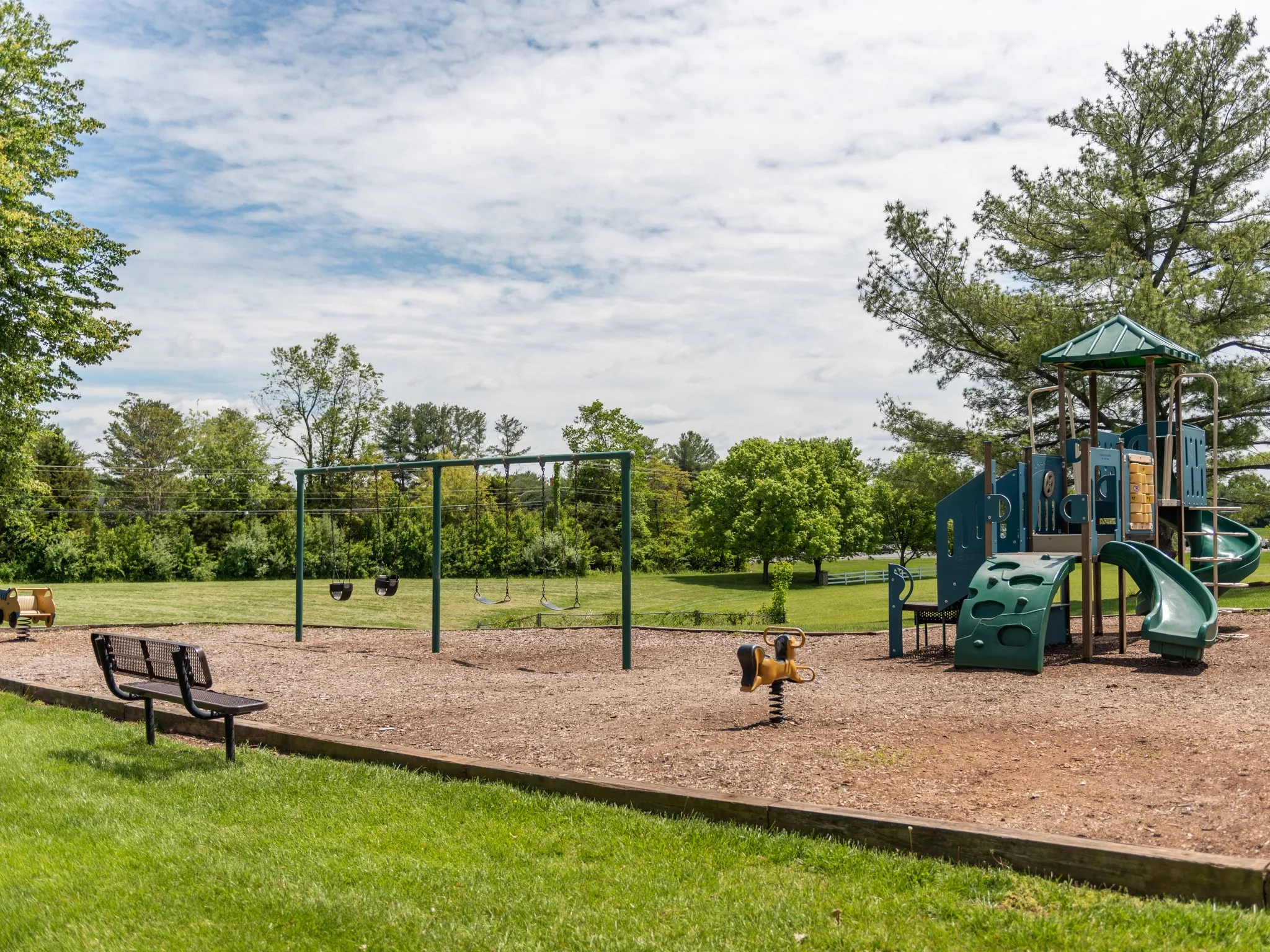 The playground at our apartments for rent in Leesburg, VA, featuring wood chips, a play structure, and a green lawn.