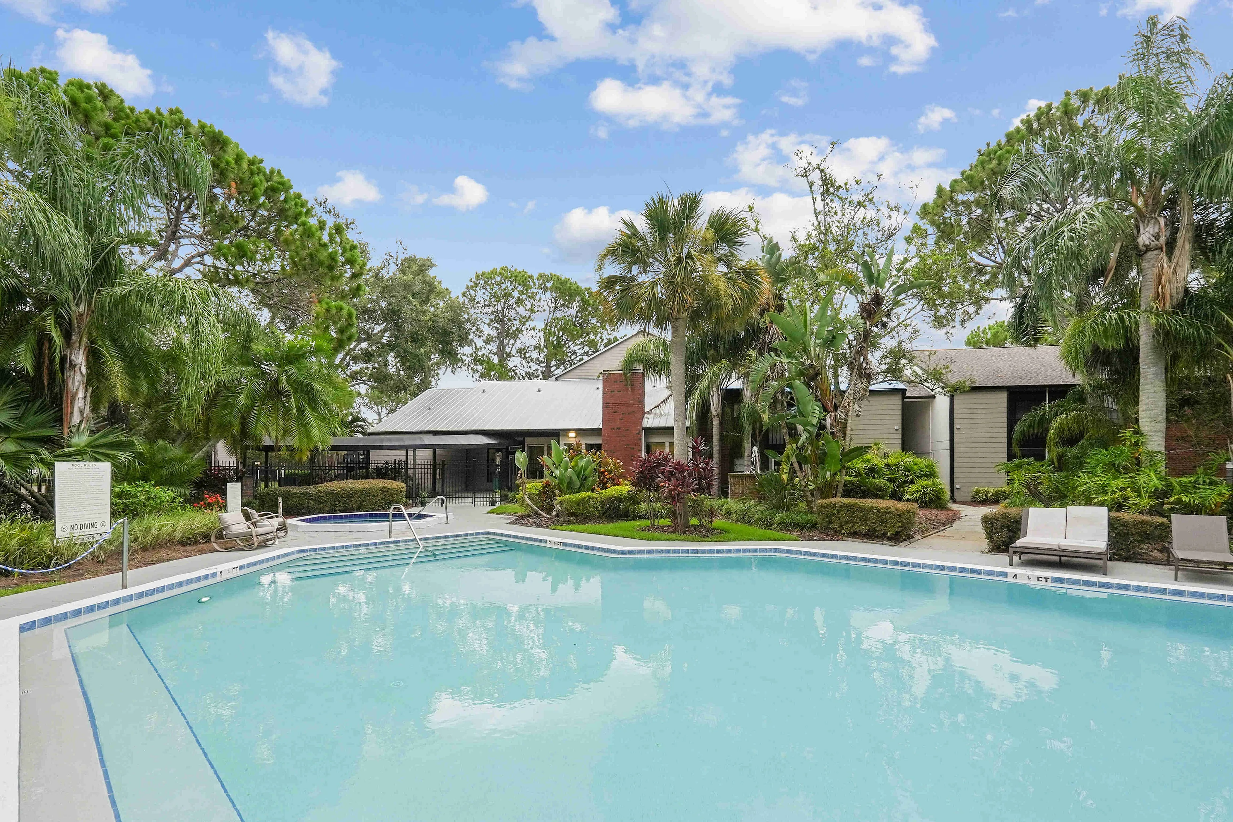 The pool area at our apartments for rent in Clearwater, FL, featuring beach chairs, umbrellas, and a hot tub.