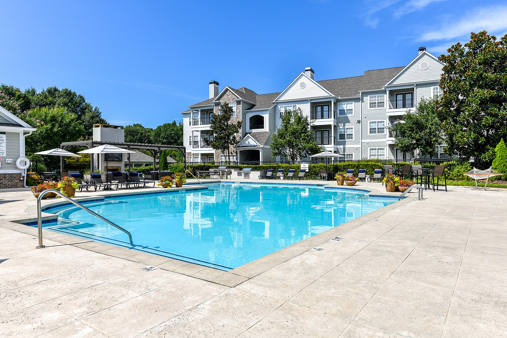 Luxurious apartment complex with a pristine swimming pool and sun loungers under bright blue skies, offering a serene environment for relaxation.