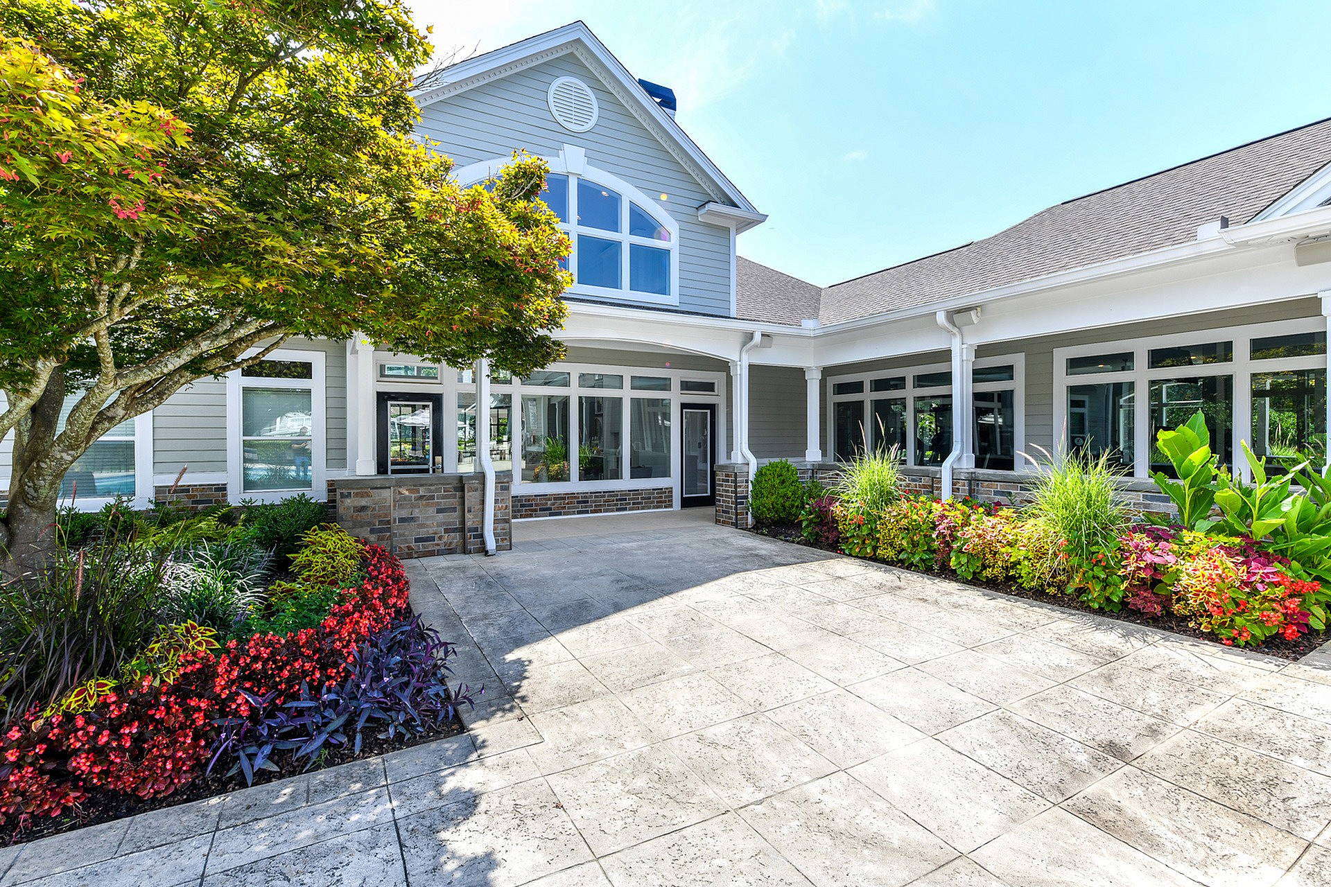 Charming modern home with expansive windows, manicured landscaping, and a welcoming front patio surrounded by vibrant flowers.