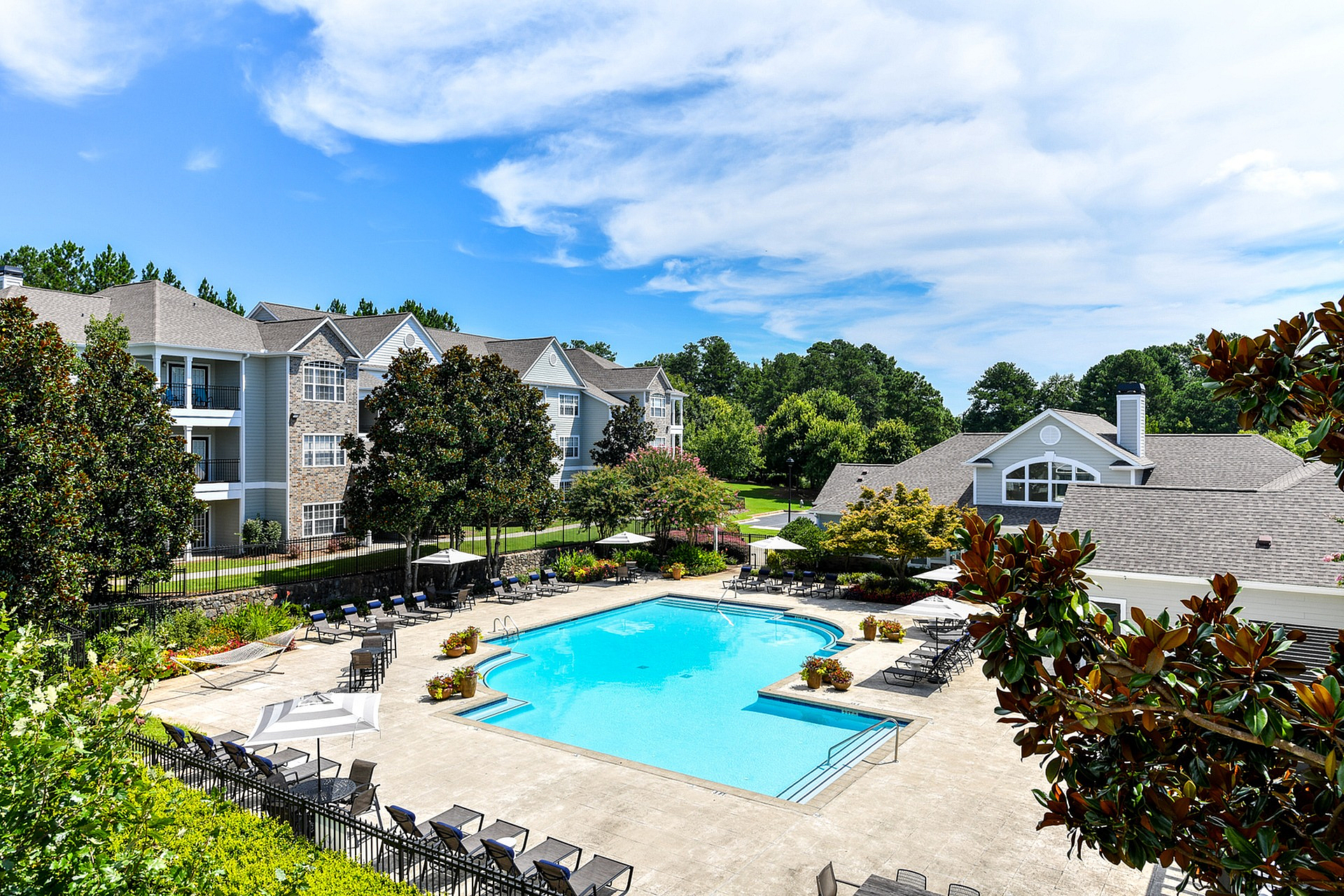 Charming apartment complex with a sparkling swimming pool surrounded by lush greenery, offering a tranquil and inviting living environment.