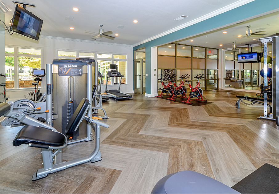 Modern fitness center with state-of-the-art equipment, including treadmills and stationary bikes, set in a spacious, bright room with stylish wood-patterned flooring.
