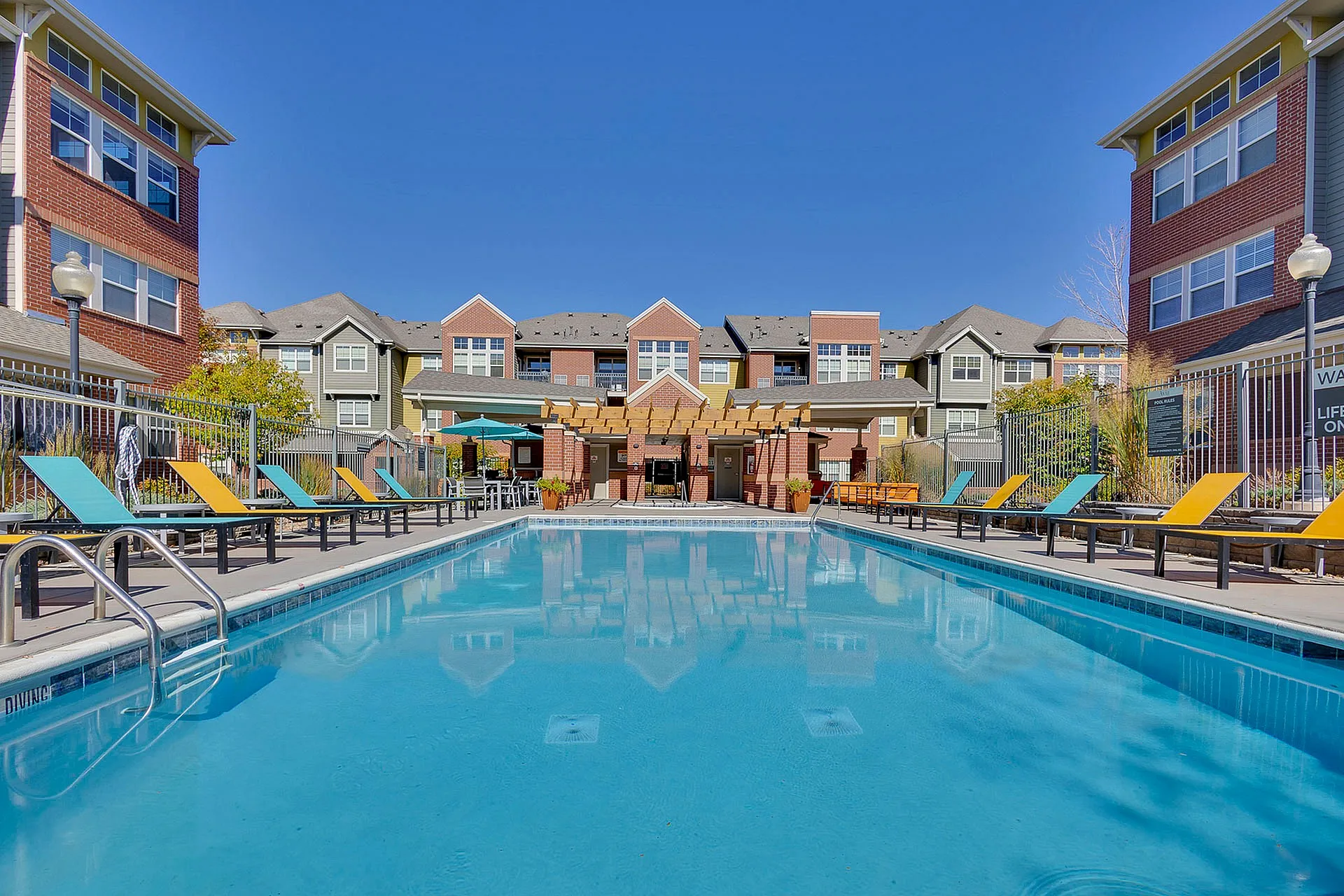 Inviting apartment complex with colorful lounge chairs by a sparkling pool, perfect for relaxation and enjoyment.