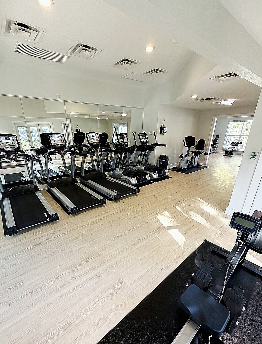 Modern fitness center with rows of sleek treadmills and exercise equipment on stylish hardwood flooring, flooded with natural light.