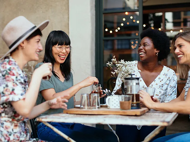 Group of friends enjoying coffee and laughter at an outdoor cafe, with a warm and inviting atmosphere.