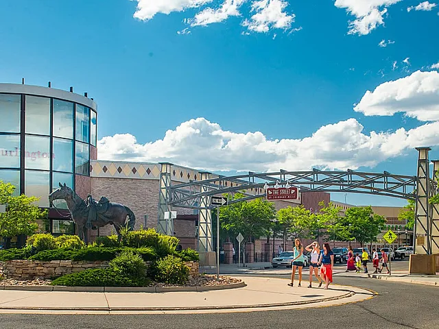Vibrant shopping district featuring a striking bronze horse sculpture, modern architecture, and families enjoying a sunny day.