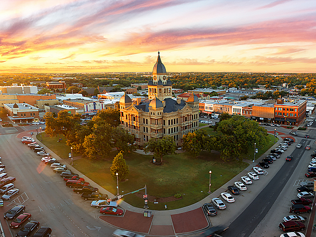 Stunning aerial view of a historic courthouse surrounded by vibrant cityscape and bustling streets at sunset.