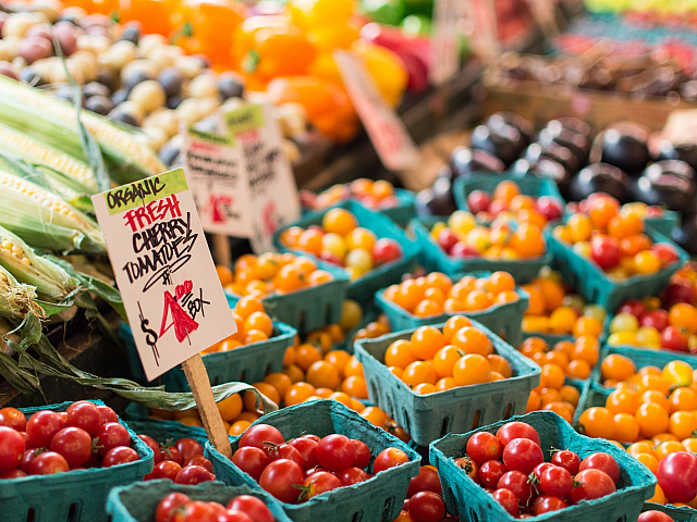 Vibrant market stall with organic fresh cherry tomatoes in blue cartons, surrounded by colorful fruits and vegetables, creating a lively and enticing shopping experience.