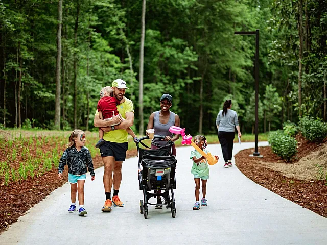 Joyful family strolling along a scenic forest path with children playing, highlighting an active and vibrant lifestyle in a lush, natural setting.