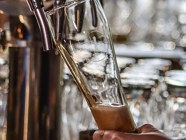Close-up of a bartender's hand expertly pouring a fresh beer from a sleek metal tap into a clear glass, showcasing a vibrant mix of craftsmanship and relaxation.