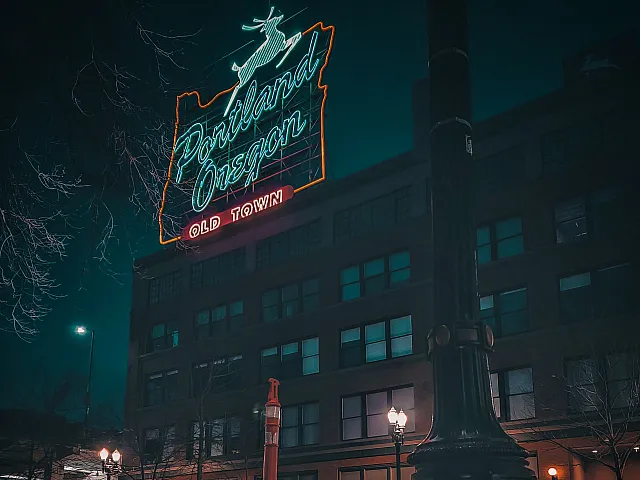 Iconic Portland Oregon neon sign illuminating the vibrant Old Town district, offering a glimpse of urban charm and historic architecture beneath a deep teal night sky.