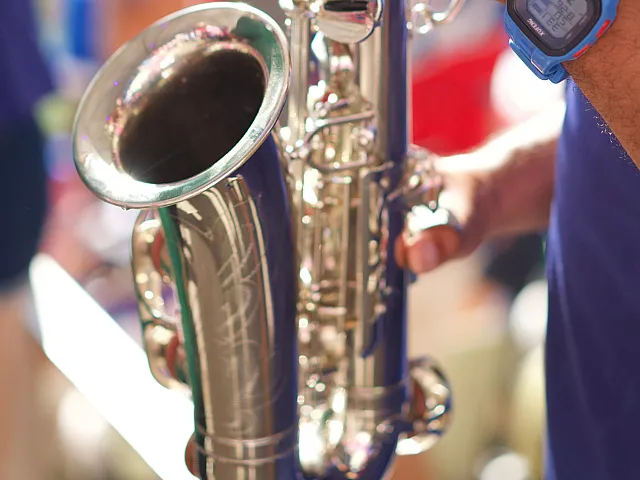 Close-up of a person playing a shiny saxophone, highlighting skilled fingers and a vibrant scene.