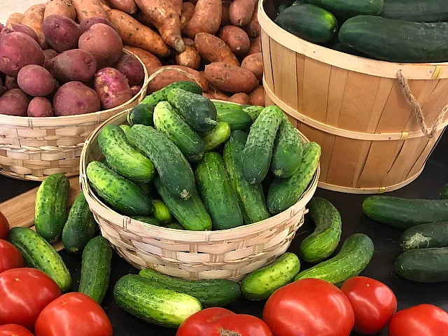 Vibrant display of fresh produce including ripe tomatoes, earthy potatoes, wholesome sweet potatoes, and crisp cucumbers in rustic baskets.